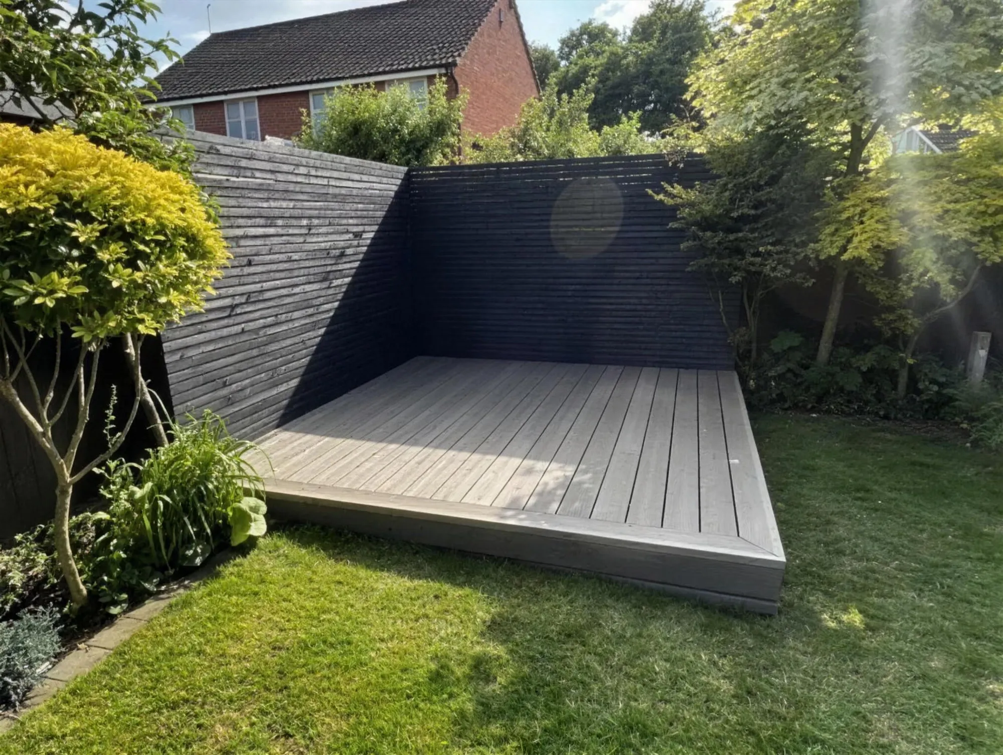 Grey composite decking in a garden corner with matching black slatted fence