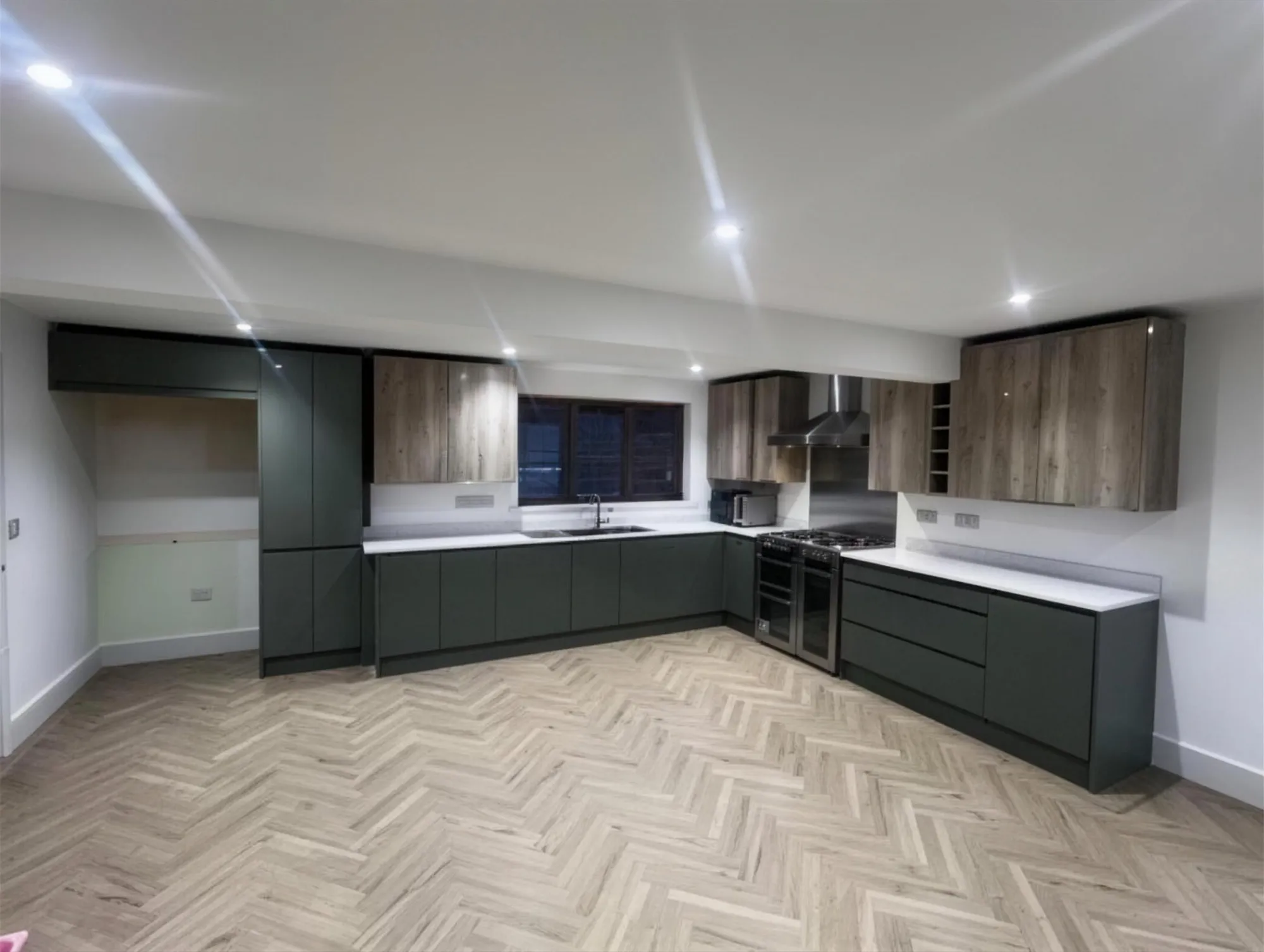 Fitted kitchen with dark green units, oak wall cabinets and herringbone LVT floor